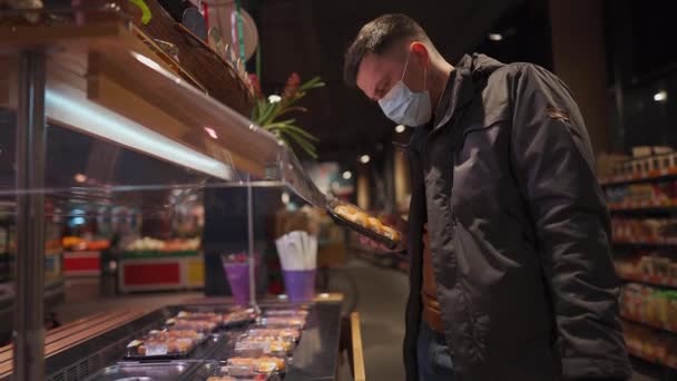 保護医療マスクの男がスーパーマーケットの棚から寿司箱を奪う 新しいノルムマスクなしのエントリ 社会的距離と隔離Covid 弁当の中で食べられる日本食 — ストック動画