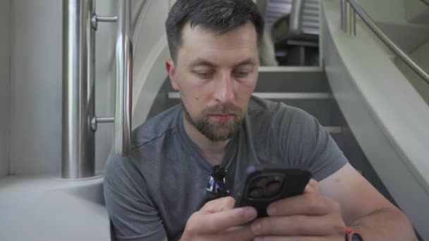 若い男は2階建ての電車に乗り スマートフォンを使ってチラシに座っている 鉄道旅行中は利用できません フライヤーとサーフィンインターネット上に座っているデュアルデッキ電車の中で男性通勤 — ストック動画