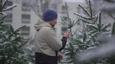 Video vlogger akıllı telefonuyla sosyal medya platformları ve takipçileri için seçtiği Noel ağacını internetten kışın karlı havalarda sokak İsa 'nın doğumu pazarında görüntüler kaydediyor.. 