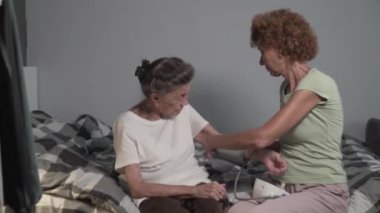 Olgun bir kadın, yaşlı bir kadının kan basıncını sphygmomanometre ile ölçmesine yardım eder. Yaşlı kız hasta yaşlı anneye bakıyor. Hemşire muayenesi hastalığı hipertansiyon.
