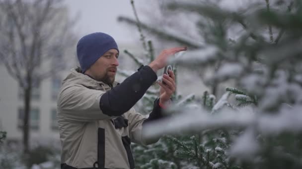 在他的智能手机上为社交媒体平台和追随者提供视频短片 内容是他选择的在冬季大雪天气下的街道圣诞树在线流媒体服务 — 图库视频影像