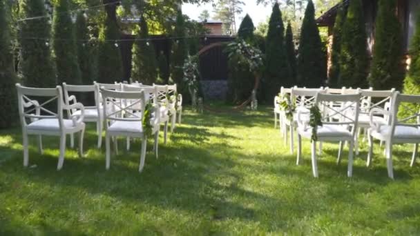 屋外の陶磁器のための結婚式の装飾 晴れた天気の緑の草の上の白い色のゲストのための結婚式のアーチそして椅子 バックヤードの結婚式場 外の結婚式の党のための家具そして装飾 — ストック動画