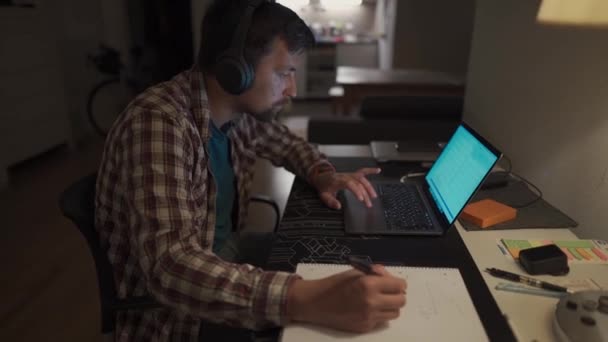 Homem Focado Fones Ouvido Com Laptop Noite Casa Tomando Notas — Vídeo de Stock