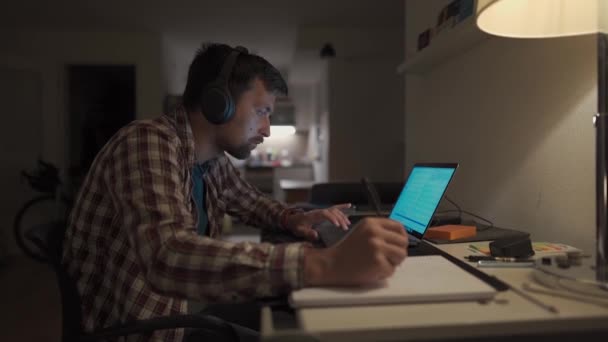 Student Doet Huiswerk Laptop Thuis Luistert Naar Muziek Koptelefoon Man — Stockvideo