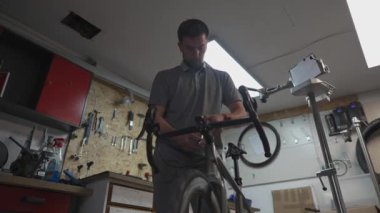 Bisiklet teknisyeni bisiklet sapını ve gidonu özel aletle büküyor. Tamirci demir cıvataları takmak için alet kullanıyor. Bisiklet servisi. İş yerinde motor tamircisi. Tamir döngüleri. Atölye. Bisikletlerin tamiri. 