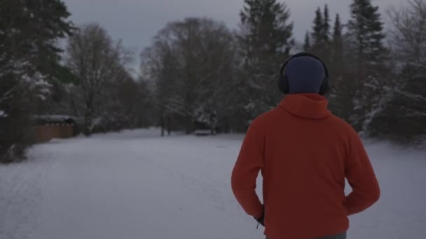 オレンジ色のスウェットシャツのバックビューで冬に雪で走る男性のジョギング 日常のアウトドアアクティブライフスタイル スポーツを楽しむ 冬に走る男のトレイルのリアビュー 凍結する雪の天気で走る — ストック動画