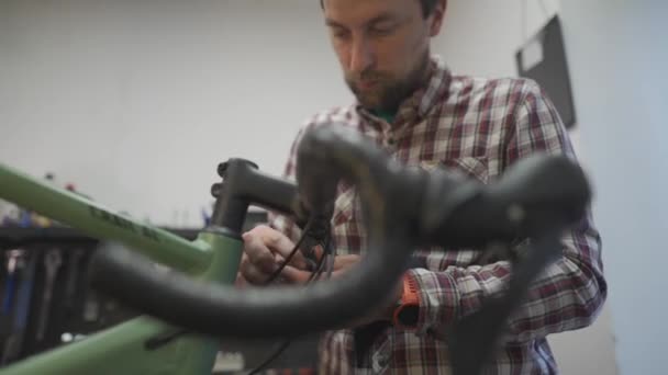 ワークショップでサイクルのハンドルバーに新しいテープを変更する自転車メカニック 自転車修理 サービスのコンセプト ハンドルバーの自転車技術者フィッティングテープ 修理工場で働くバイク修理士 — ストック動画