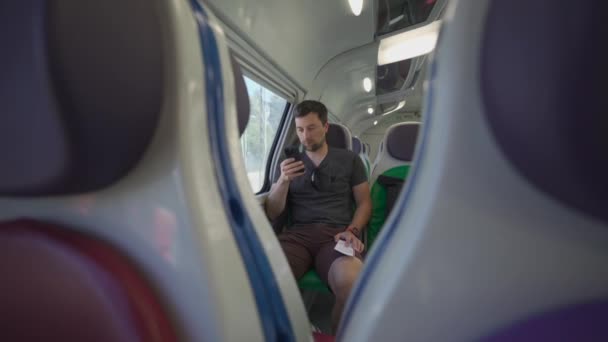 在意大利罗马的一个阳光明媚的夏日 年轻人坐着一辆空荡荡的意大利火车 车上坐着五颜六色的座位 手里拿着车票 旅客在铁路检查路线上乘坐电话 — 图库视频影像