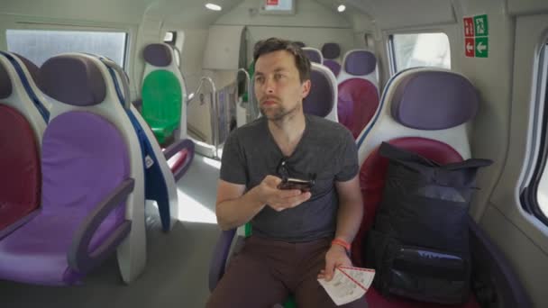 在意大利罗马的一个阳光明媚的夏日 年轻人坐着一辆空荡荡的意大利火车 车上坐着五颜六色的座位 手里拿着车票 旅客在铁路检查路线上乘坐电话 — 图库视频影像
