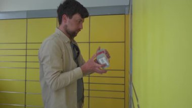 Paketleme istasyonundaki adam ekranı kullanıyor ve kendini sevkiyat için kutuyu tutuyor. Paket teslimat noktası, paket teslimatı, paket teslimatı. Sarı self-servis terminal makinesi. Depo için depozit. 