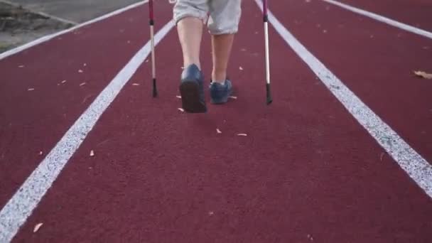 一名老年妇女的腿在体育场的跑道上走着 可以看到北欧步行杆的后视镜 老年人的积极生活方式和有氧耐力运动与运动手杖 斯堪的纳维亚人走路 — 图库视频影像