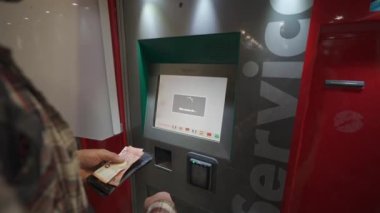Roma. İtalya. Roma Fiumicino Havaalanı 'ndaki kırmızı renkli tren istasyonunun self-servis bilet makinesinden bilet alan bir adam. Trenitalia otomatik bilet otomatı. Bilet büfesi. 