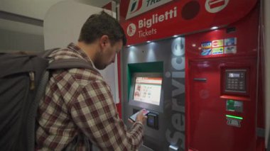 7 Ekim 2023. Roma. İtalya. Roma Fiumicino Havaalanı 'ndaki kırmızı renkli tren istasyonunun self-servis bilet makinesinden bilet alan bir adam. Trenitalia otomatik bilet otomatı. Bilet büfesi. 