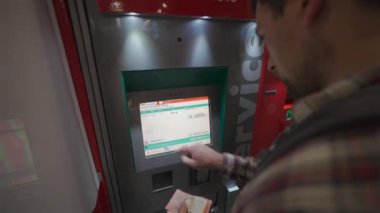 Roma. İtalya. Roma Fiumicino Havaalanı 'ndaki kırmızı renkli tren istasyonunun self-servis bilet makinesinden bilet alan bir adam. Trenitalia otomatik bilet otomatı. Bilet büfesi. 