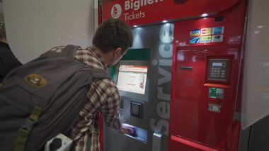 7 Ekim 2023. Roma. İtalya. Roma Fiumicino Havaalanı 'ndaki kırmızı renkli tren istasyonunun self-servis bilet makinesinden bilet alan bir adam. Trenitalia otomatik bilet otomatı. Bilet büfesi. 