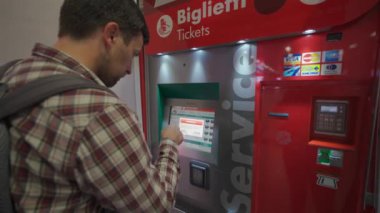 7 Ekim 2023. Roma. İtalya. Roma Fiumicino Havaalanı 'ndaki kırmızı renkli tren istasyonunun self-servis bilet makinesinden bilet alan bir adam. Trenitalia otomatik bilet otomatı. Bilet büfesi. 