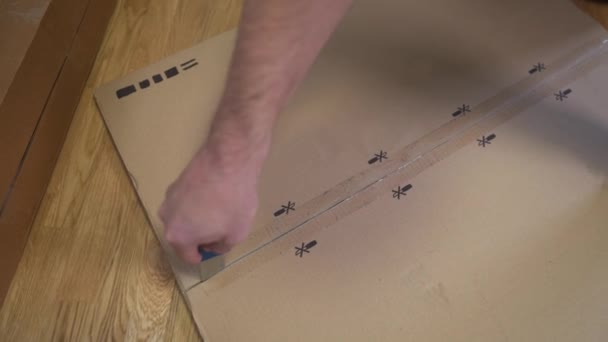 男は床にテーブルを組み立てるためにナイフで部品の段ボール箱を発見しました 自分で家具の組み立て 白い箱はあなた自身の家具それをする 購入者はすぐに組み立てられる折りたたみテーブルを収集します — ストック動画