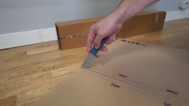 床にナイフで自己組立のための分解家具の男のアンパックボックス 男性は包装と折り目テーブルを削除します 段ボール箱 アセンブリのための新しい家具や継手付きパッケージ — ストック動画