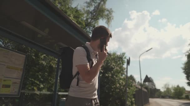 Frustrated man waits for bus that is delayed at halt and calls on his mobile phone. Passenger gets angry and waits long time for public transport at a stop in Germany. Traffic delays and lateness. 