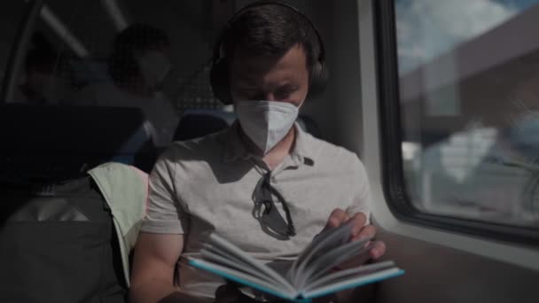 男の乗客はヘッドフォンを着用し 本を読んで夏にドイツの郊外電車に乗っています 学生は電車の中で無線電話の教科書を読みます 教育への毎日の通勤 — ストック動画