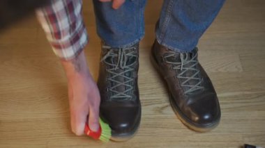 Tanınmayan adam kahverengi deri botları fırçayla temizliyor ve krem sürerek kayganlaştırıcı sürüyor. Temalı ayakkabı bakımı. Acemi cilası. Açık hava botları ve balmumu. Çizme bakımı için aksesuarlar. 