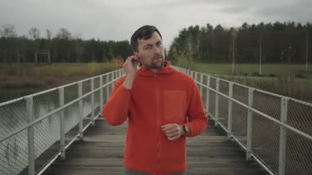 在自然小径上练习跑步时 在耳机中听音频播客和有声读物或音乐 跑步者戴上有线耳机 在秋天开始户外运动训练 — 图库视频影像