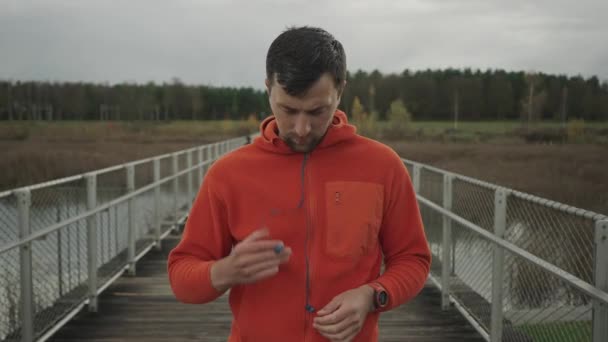 在户外运动前 男性跑步者要戴上频道内有线耳机 男子慢跑者穿着耳机准备跑步 在跑步锻炼时听音乐 带着音乐慢跑 — 图库视频影像