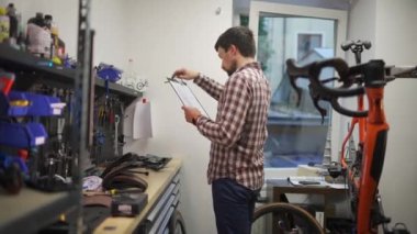 Bisiklet teknisyeni idari işler yapıyor. Motosiklet tamircisi iş belgelerini notlar. Bisiklet mühendisi iş başında. Araç tamircisi kayıtları atölyedeki panoda çalışıyor. Kalite kontrol süreci. 