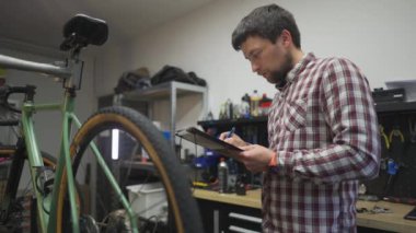 Bisiklet teknisyeni idari işler yapıyor. Motosiklet tamircisi iş belgelerini notlar. Bisiklet mühendisi iş başında. Araç tamircisi kayıtları atölyedeki panoda çalışıyor. Kalite kontrol süreci. 