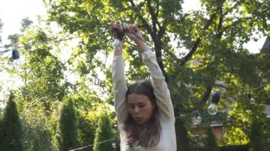 Kadın dekoratör bahçede yapılacak düğün törenleri için siyah tel çelenkler hazırlıyor. Kadın tasarımcı açık hava ışığını düğün töreni için hazırlıyor. Düğün kemerinde çiçekler ve lambalar ile dekorasyon. 