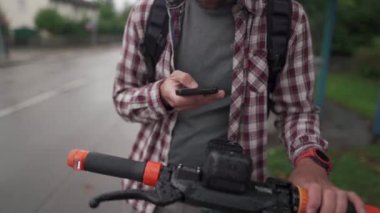 Adam şehirde elektrikli scooter kiralamak için akıllı telefon kullanıyor. Genç adam e-scooter 'ın parasını cep telefonuyla internet üzerinden ödüyor. Elektrikli araç kiralama teması. Kentsel çevre dostu ulaşım. 