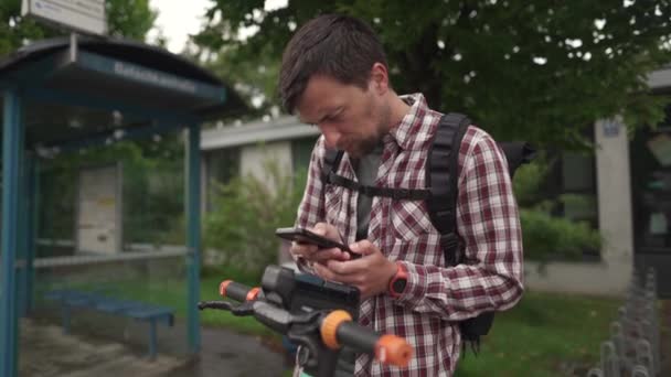 Man uses smartphone to rent an electric scooter in city. Young guy paying for e-scooter via online payment using his mobile phone. Theme of electric vehicle rental. Urban eco-friendly transport. 
