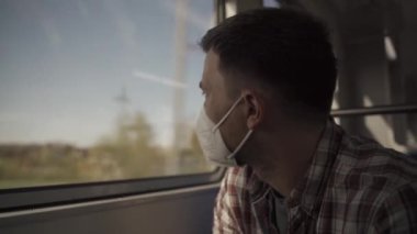 Maskeli adam, hareket halindeki bir trenin penceresinden dikkatlice dışarı bakar. Üzgün erkek eve doğru ilerliyor, pencerede oturuyor ve düşünüyor. Seyahat eden kişi kavramı. Almanya 'da demiryolu. Kişisel koruma. 