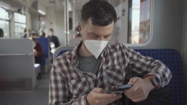 KN95 FFP2 yüz maskeli adam Almanya 'da bir banliyö trenine biner ve akıllı telefonuyla interneti gezer. Trende seyahat eden maskeli bir erkek ve internette sörf yapıyor. Toplu taşımada iyi yolculuklar.. 