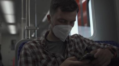 Adam Almanya 'da banliyö trenine koruyucu maske takarak biniyor ve güneşli havada akıllı telefon kullanıyor. Cep telefonlu gezgin cep telefonu uygulaması, sosyal medya ya da trendeki internet bilgileri. 
