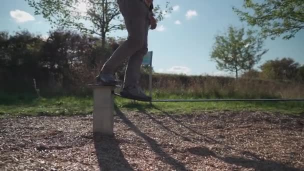 スニーカーの男はドイツの公園でゴムからロープのバランスを学び 歩くことを学びます スポーツ レジャー レクリエーション 健康的なアクティブなライフスタイルのコンセプト 初心者はスラックラインで屋外でバランス — ストック動画
