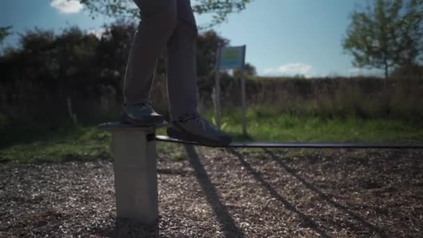 スニーカーの男はドイツの公園でゴムからロープのバランスを学び 歩くことを学びます スポーツ レジャー レクリエーション 健康的なアクティブなライフスタイルのコンセプト 初心者はスラックラインで屋外でバランス — ストック動画