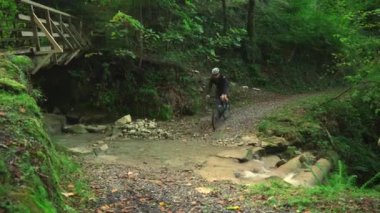 Erkek bisikletçi dağlarda çakıllı bisikletle nehri geçiyor. Bisikletli turist bisikletçisi sonbaharda ormanda dağ nehrinden geçer. Motosiklet macerası. Bisikletçi bisikletle dağ akıntısını geçiyor.. 