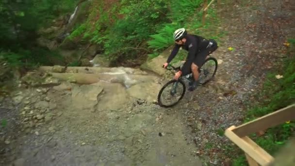 砂利自転車の山で川を渡る男性サイクリスト 自転車ツーリストのバイクパッカーは 秋に森で山の川を渡ります バイクアドベンチャー 自転車はサイクルで山の流れを横断する — ストック動画