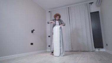 Mutlu yetişkin kadın yeni ortopedik yatağını açıyor. Makasla dolu yatağı torbaya boşalt. Yeni daireye taşınıyorum. Mobilyasız yeni ev. Yaşlı kadın evde yatak açıyor..