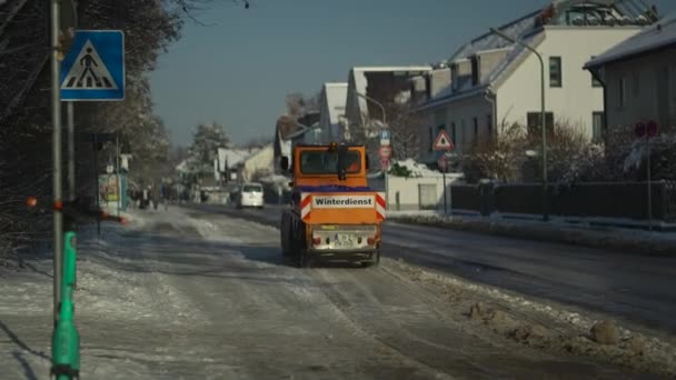オレンジマシンは雪が降った後の晴れた天気でドイツのミュンヘンの舗装とサイクルウェイから高速でバケツで雪をシャベルします ドイツのウィンターハウス フットパスから雪を遮るトラクター — ストック動画
