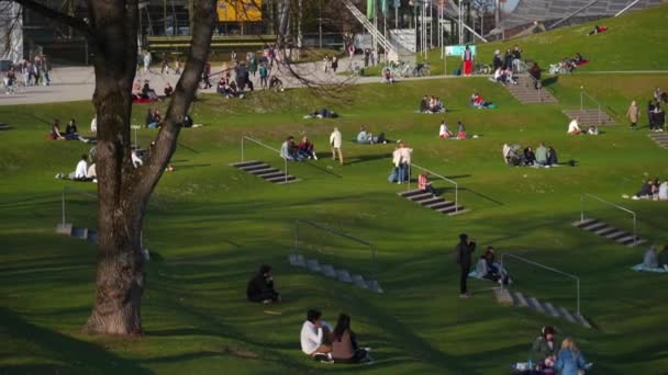 2022年3月25日 ミュンヘン ドイツ 人々は暖かい晴れた春の天気でミュンヘンの湖近くのオリンピック公園で緑の草でリラックスします オリンピアパーク ミュンヘン オリンピア オリンピア パーク オリンピア — ストック動画