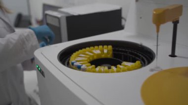 Üniformalı laboratuar teknisyeni kan örneklerini otomatikleştirilmiş robot makineye yerleştiriyor. Biyolojik sıvıların analizi için klinik kimya çözümleyicisi numunelerin incelenmesi için tıbbi laboratuvar ekipmanları için.. 
