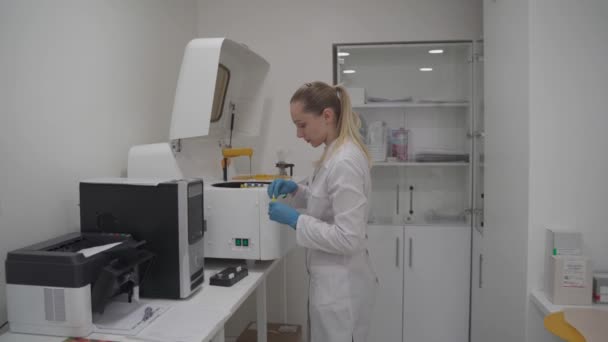 制服化验室技术员将血液样本放入用于分析生物液体的自动化机器人 用于检测样本的临床化学分析器 医疗实验室设备 — 图库视频影像