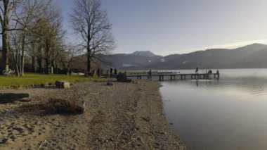  Tegernsee Gölü, Bavyera, Almanya. İnsanlar güneşli bahar günlerinde göl kıyısında ve Bavyera Alpleri 'ne bakan iskelede dinleniyorlar. İnsanlar ilk güneşli günleri göl kenarında yakalar.. 
