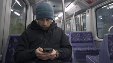 Hamburg 'da metroda seyahat eden mavi koltukta oturan ve kışlık kıyafetler giymiş akıllı telefon kullanan bir adam. Hamburg metro banliyösü işe gidip gelirken internette geziniyor. Hamburger U-Bahn. 