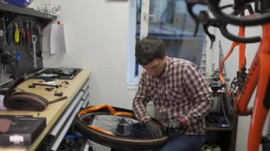 Bisiklet tamircisi bisiklet tamir atölyesinde çok hafif turuncu bisiklet tüpü ve tekerlek takıyor. Tamirci bisiklet tüpünü değiştiriyor ve tamircide bisiklet tekerleğini tamir ediyor. Çalışma İstasyonu. 