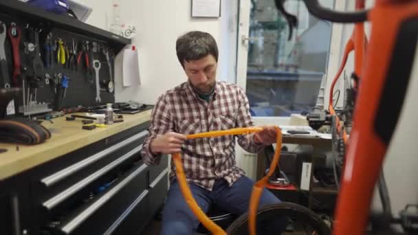自行车技工在自行车修理厂安装了非常轻的橙色自行车管 并在自行车车轮上安装了轮胎 修理工在维修车间更换自行车轮毂 修理自行车轮毂 工作站 — 图库视频影像
