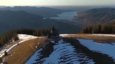 Kapelle Heilig Kreuz Rottach-Egern Tegernsee. Wallbergkapelle, Tegernsee Gölü 'ne tepeden bakan Wallberg Dağı ve güneşli bahar havasında gün batımında karla kaplı dağ sıraları. Alplerin zirvesindeki şapel. 