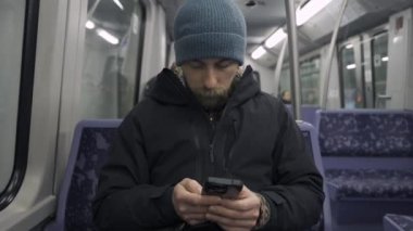 Hamburg 'da metroda seyahat eden mavi koltukta oturan ve kışlık kıyafetler giymiş akıllı telefon kullanan bir adam. Hamburg metro banliyösü işe gidip gelirken internette geziniyor. Hamburger U-Bahn. 